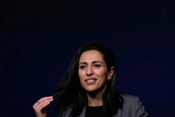 Femme souriante en veste grise sur fond bleu.