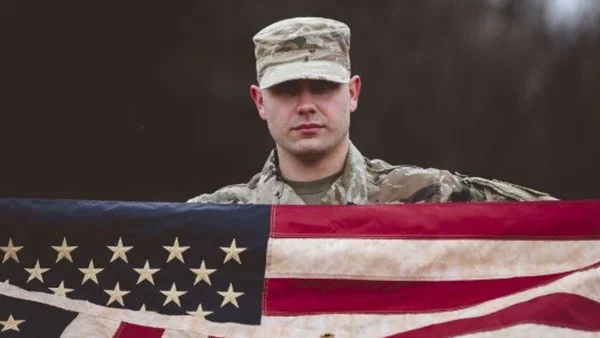 Un militaire américain en tenue de camouflage devant un drapeau américain patiné.