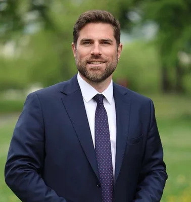Vincent Jeanbrun souriant en costume et cravate à pois, debout à l'extérieur.