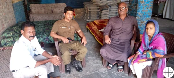 Un homme en uniforme, une femme en voile coloré et deux autres hommes discutant dans une pièce simple.