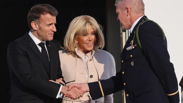 Emmanuel Macron et une femme en manteau clair saluant un militaire lors d'une cérémonie.