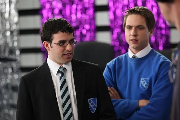 Simon Bird et Joe Thomas posant devant des décorations de guirlandes violettes.