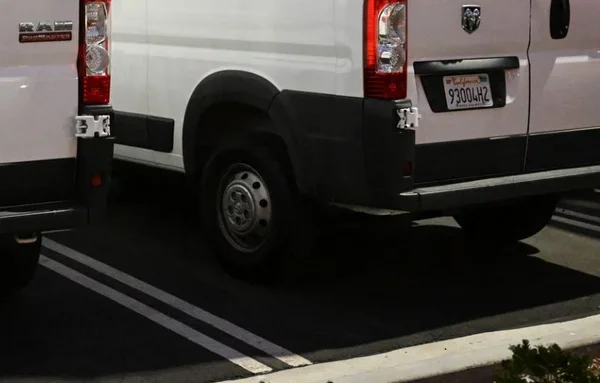 L'arrière de deux camionnettes blanches stationnées sur un parking bitumé.