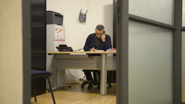 Un homme assis à son bureau en train de téléphoner et de prendre des notes.