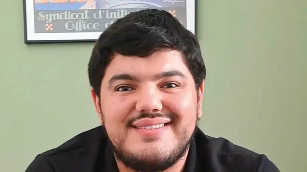 Portrait de Mehdi Kessaci souriant devant un mur vert.