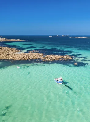 Paysage côtier de l'Iroise avec ses rochers, son eau turquoise et un bateau amarré près de la côte.