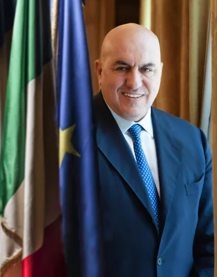 Guido Crosetto photographié officiellement devant les drapeaux italien et européen.