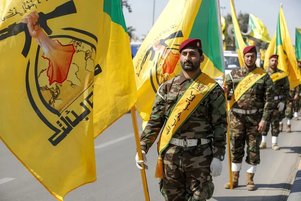 Un militaire portant le patch du drapeau français en observation devant des structures industrielles en zone désertique.