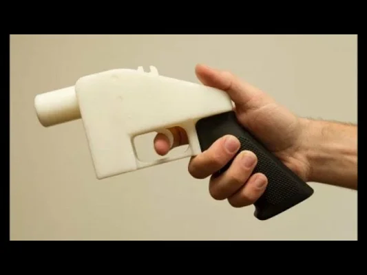 Une arme à feu imprimée en 3D avec un corps blanc et une poignée noire texturée, tenue en main.