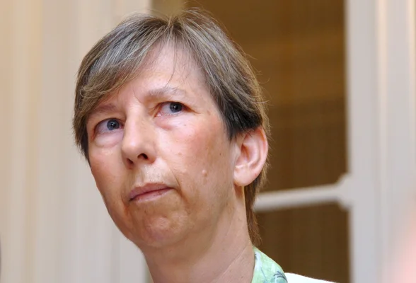 Portrait d'une personne aux cheveux courts portant une chemise vert clair, devant un fond intérieur neutre.