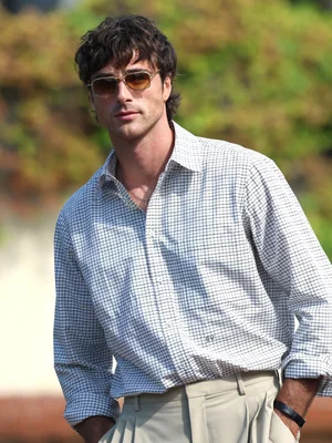 Jacob Elordi portant une veste noire et une chaîne en or devant un fond lumineux flou.