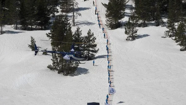 Hélicoptère et personnes sur un site enneigé dans les Alpes.