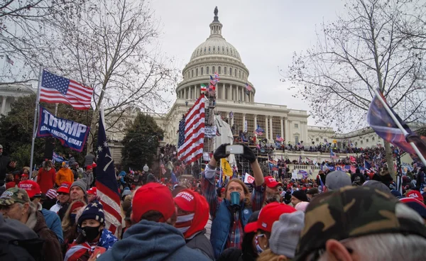 Partisans de Donald Trump lors de l'assaut du Capitole le 6 janvier, drapeaux américains et bannières à l'avant-plan.