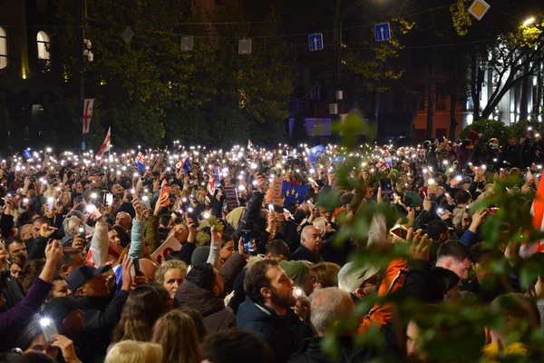Manifestants géorgiens utilisant leurs téléphones portables pour éclairer la foule lors d'un rassemblement nocturne.