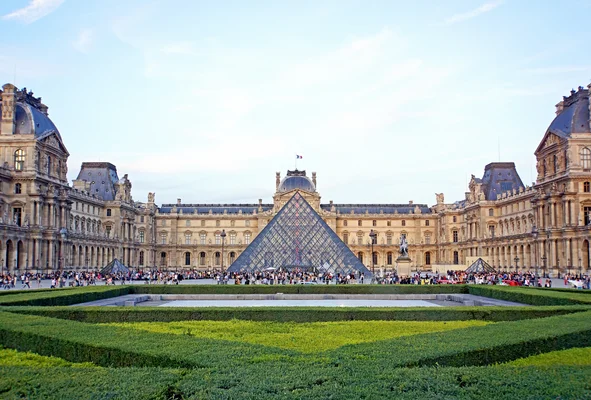 La pyramide du Louvre entourée des bâtiments historiques, avec visiteurs et jardin géométrique en avant-plan.