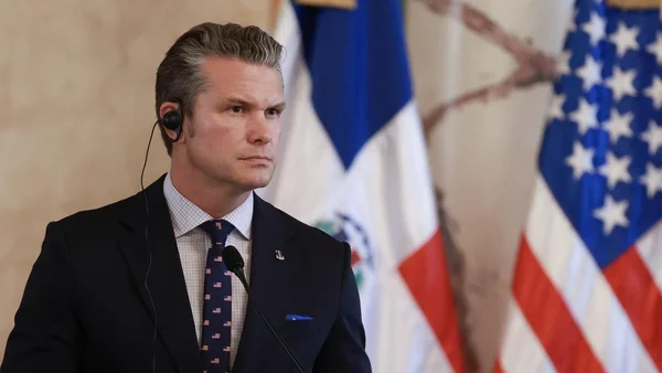 Pete Hegseth s'exprimant devant des micros, avec les drapeaux du Salvador et des États-Unis en fond.