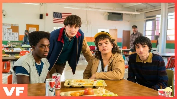 Quatre jeunes personnages assis à une table de cafeteria avec un drapeau américain.