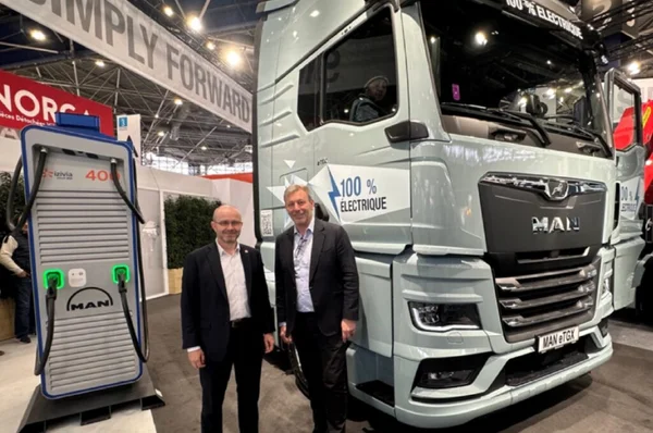 Deux hommes devant un camion électrique MAN eTGX et une borne de recharge.
