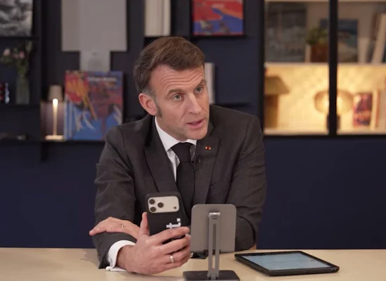 Emmanuel Macron tenant un smartphone, posant à côté d'une tablette sur un bureau