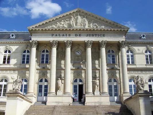 Extérieur du palais de justice avec son architecture classique, ses colonnes et son horloge.