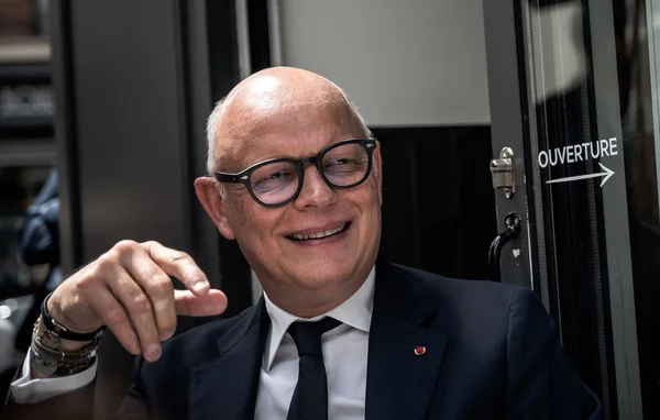 Édouard Philippe souriant et gestuant à côté d'une porte signalisée 'OUVERTURE'.