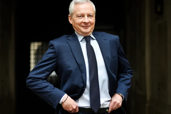 Portrait de Bruno Le Maire dans un costume bleu marine, souriant face à l'objectif.