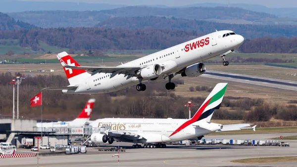 Un avion Swiss décollant au-dessus d'un avion Emirates sur le tarmac.