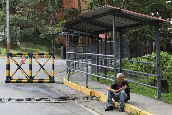 Julien Février assis sur un trottoir près d'une bordure jaune, portant un t-shirt noir et un jean bleu clair.