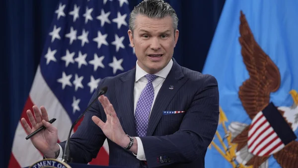 Pete Hegseth s'adressant à la presse depuis un pupitre officiel, flanqué des drapeaux américain et du département de la Défense.