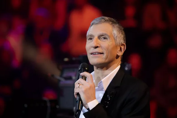 Nagui en costume tenant un micro lors d'une prestation.