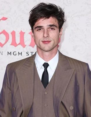 Portrait rapproché de Jacob Elordi avec moustache légère et blazer sombre.