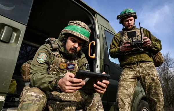 Deux soldats manipulant une tablette et une télécommande de drone près d'un véhicule militaire en Ukraine.