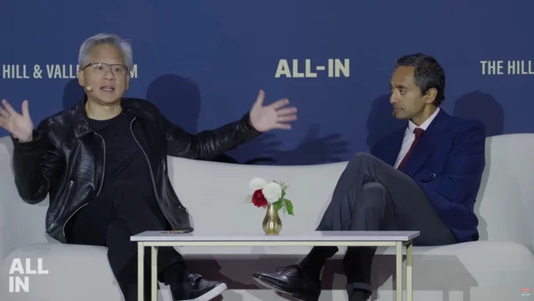 Mark Zuckerberg et Jensen Huang installés sur un canapé bleu lors d'un événement intitulé 'ALL-IN'.