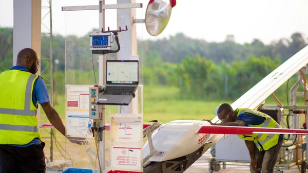 Un drone Zipline décollant d'une plateforme face à un paysage de collines vertes.