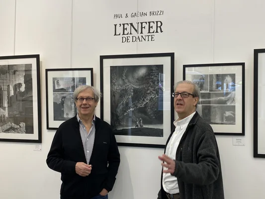 Paul et Gaëtan Brizzi debout devant des cadres de L'ENFER DE DANTE exposés au mur.