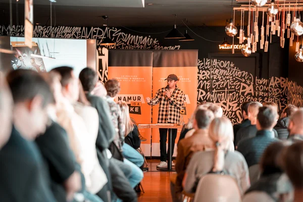 Une présentation lors du festival Namur is a joke dans une salle décorée de graffitis.