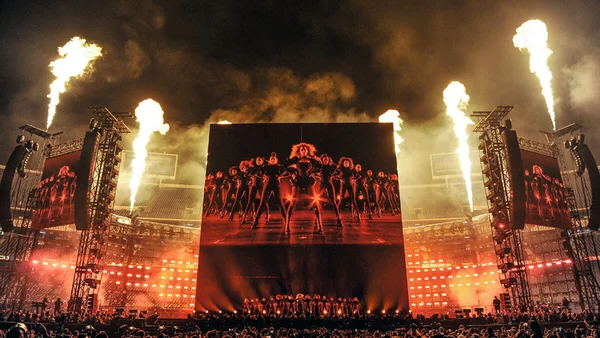 Une scène de concert en pleine nuit avec des effets de flammes et de lumières rouges.