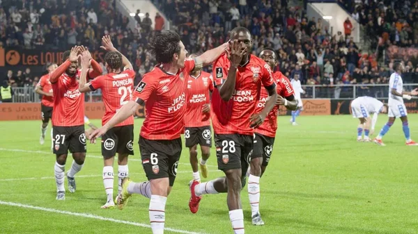Les joueurs du FC Lorient célébrant ensemble sur la pelouse devant les supporters.