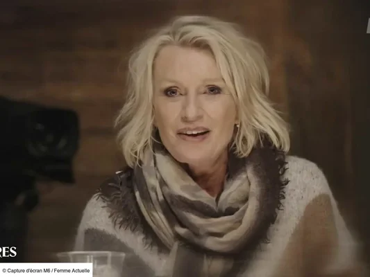 Gros plan sur Sophie Davant en haut clair et écharpe à motifs dans un décor aux tons chauds.