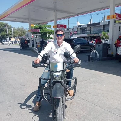 Julien Février assis sur une moto à une station-service, vêtu d'une chemise blanche et d'un jean.