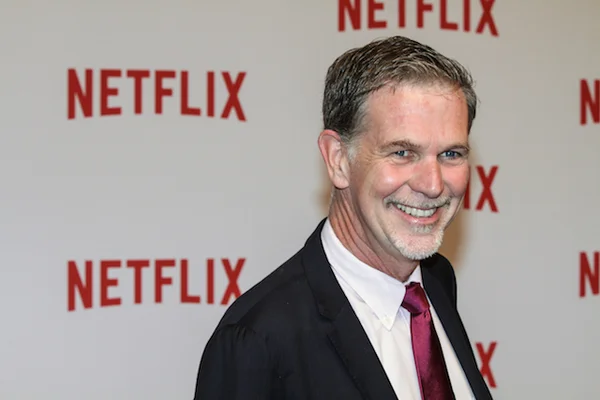 Reed Hastings posant devant les logos de Netflix.