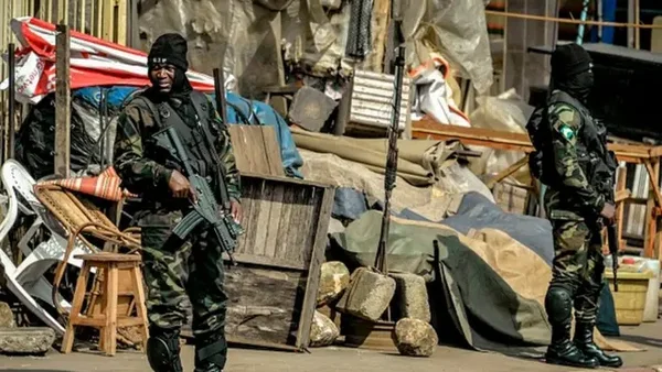 Hommes armés en camouflage dans un environnement extérieur désorganisé.