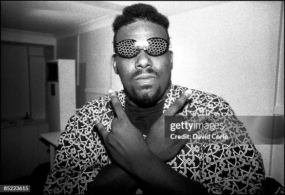 Afrika Bambaataa à l'intérieur, portant des lunettes originales et un chemisier à motifs.