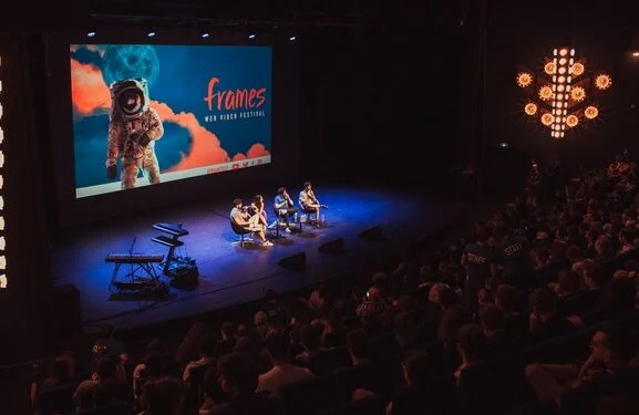 Table-ronde sur la scène du Frames Festival avec un écran géant et éclairages d'ambiance.