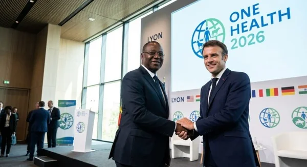Poignée de main entre le président Mahama et Emmanuel Macron devant l'écran du sommet One Health 2026 à Lyon.