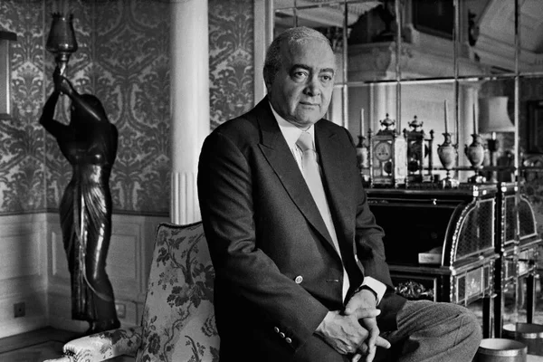 Portrait officiel de Mohamed Al-Fayed assis dans un intérieur décoré.