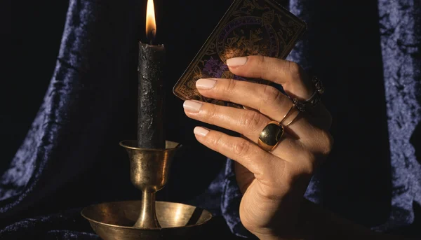 Main de femme tenant une carte de tarot illuminée par la flamme d'une bougie, ambiance mystérieuse et sombre