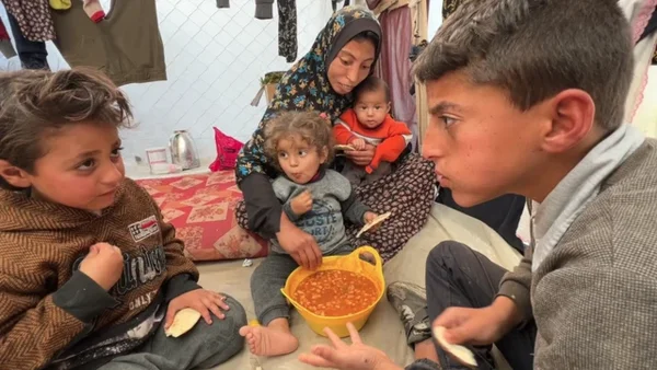Enfants palestiniens de Gaza partageant un repas avec une femme dans un espace précaire.