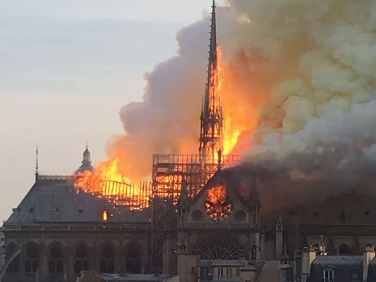 Notre-Dame de Paris en flammes, la flèche partiellement effondrée et la rosace visible à travers la fumée.