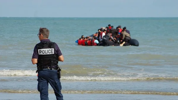 Un policier faisant face à la mer où un migrant en gilet orange tente de nager.